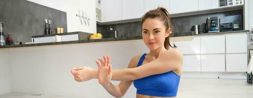 jong vrouw doet training van huis, zit Aan yoga mat en strekt zich uit haar handen, geschiktheid opleiding sessie in leven kamer foto