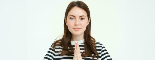 portret van jong vrouw drukt uit haar dankbaarheid, shows dank jij, namaste gebaar, Holding handen geklemd samen in de buurt borst en lachend, staand over- wit achtergrond foto