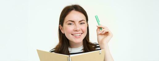 beeld van mooi jong vrouw, leerling Holding notitieboekje, memo ontwerper en pen, glimlachen en op zoek Vrolijk, geïsoleerd tegen wit achtergrond foto