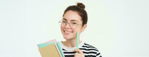 portret van slim meisje in bril, tutor Holding pen en notitieboekjes, leerling dragen haar huiswerk notities, staand over- wit achtergrond foto