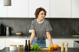 portret van glimlachen schattig jong vrouw maken ontbijt, hakken groenten in de keuken, voorbereidingen treffen veganistisch maaltijd foto