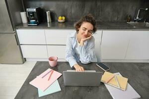 mooi eigen baas meisje werken van huis. jong vrouw online aan het studeren, aan het kijken Cursus Aan website, op zoek Bij laptop scherm foto