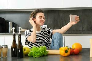 schattig jong vrouw, modern levensstijl blogger, nemen selfie terwijl Koken salade in de keuken, gebruik makend van smartphone naar maken foto's voor sociaal media app foto