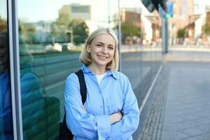 levensstijl portret van jong glimlachen vrouw, leerling of kantoor medewerker, staand Aan straat in blauw shirt, kruis armen Aan borst en op zoek zelfverzekerd Bij camera foto