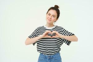 portret van mooi meisje shows hart teken, liefde gebaar, Leuk vinden iets, staat over- wit achtergrond foto