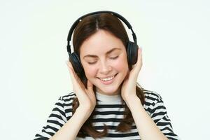 portret van vrouw, lachend, vervelend draadloze koptelefoon, luisteren muziek, aan het studeren in oortelefoons, staand geïsoleerd over- wit achtergrond foto