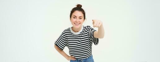 beeld van elegant jong vrouw, richten vinger Bij camera, uitnodigend jij, staand over- wit achtergrond foto