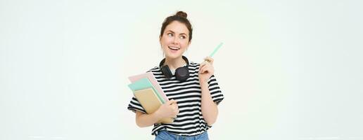 portret van jong vrouw, leerling met notebooks en oortelefoons Aan haar nek, poseren voor college advertentie, wit achtergrond foto