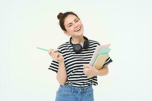 portret van jong vrouw, leerling met notebooks en oortelefoons Aan haar nek, poseren voor college advertentie, wit achtergrond foto