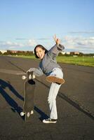 verticaal schot van gelukkig Aziatisch schaatser meisje, springen, staand met skateboard en lachend. vrouw het schaatsen Aan longboard en hebben pret foto