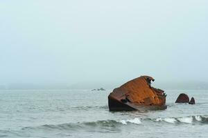 oud schipbreuk, fragmenten van een schip gewassen aan wal tegen een mistig zeegezicht foto