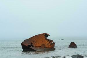 roestig schipbreuk, stoffelijk overschot van een schip gewassen aan wal tegen een mistig zeegezicht foto