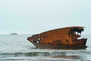 roestig schipbreuk tegen een mistig zeegezicht met een schip in de afstand foto