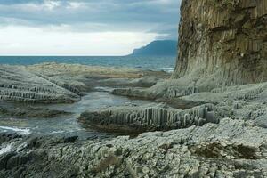 rotsachtig kust gevormd door zuilvormig basalt tegen de backdrop van een stormachtig zee, kust- landschap van de koeril eilanden foto