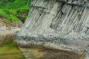 voet van een kust- klif samengesteld van zuilvormig basalt, Aan de eiland van kunashir foto