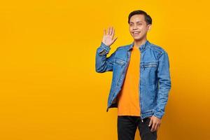 portret van glimlachende Aziatische jonge man die lege ruimte begroet op gele achtergrond foto