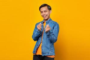 portret van glimlachende jonge aziatische man die vingerhart over gele achtergrond toont