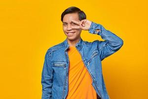 portret van vrolijke jonge Aziatische man die vredesteken maakt met vingers over gele achtergrond