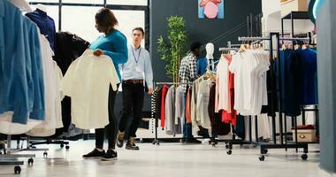 Afrikaanse Amerikaans klant analyseren overhemd kleding stof in modern boetiek, boodschappen doen voor modieus handelswaar. elegant vrouw willen naar kopen modieus kleren voor nieuw garderobe in kleding op te slaan. mode concept foto