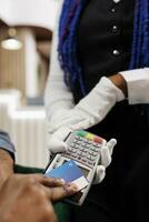 Mens maken betaling gebruik makend van contactloos credit kaart, detailopname van hand- betalen Bill bestellen met nfc technologie terwijl resting Bij hotel lounge Oppervlakte. serveerster vervelend wit handschoenen Holding pos terminal foto