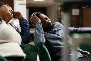 moe ongelukkig Afrikaanse Amerikaans familie paar slaap in hotel lobby hebben Jet vertraging symptomen, toeristen gevoel slaperig en uitgeput na lang vlucht. lucht reizen en slaap ontbering foto