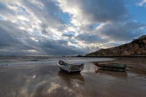 een kleine boot aangemeerd op het bewolkte strand, en de lucht was bedekt met donkere wolken foto
