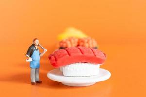 kleine chef-kok die sushi maakt op een oranje achtergrond foto