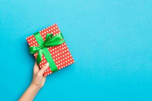 vrouw armen Holding geschenk doos met gekleurde lint Aan blauw tafel achtergrond, top visie en kopiëren ruimte voor u ontwerp foto