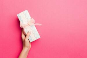 meisje handen Holding ambacht papier geschenk doos met net zo een Cadeau voor Kerstmis of andere vakantie Aan roze achtergrond, top visie met kopiëren ruimte foto