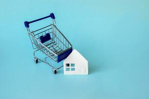 mini boodschappen doen trolley met een wit huis Aan een blauw achtergrond. foto