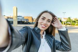 blauwe ogen blond vrouw in leer jasje glimlachen duurt een selfie met haar camera in de straat foto