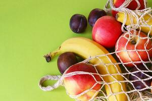 rood appels, bananen, pruimen en draad zak Aan een helder groen achtergrond. foto