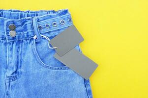 vlak leggen, detail van denim jeans met blanco grijs etiket Aan geel achtergrond. foto
