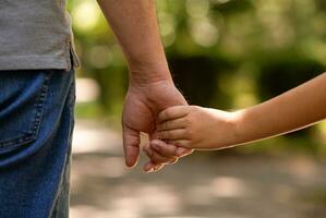 de vader hand- gehouden strak de hand- van zijn weinig zoon tegen de achtergrond van groen gebladerte, detailopname foto