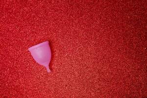 roze menstruatie- kop Aan glimmend rood achtergrond, boven visie. nul verspilling concept. milieuvriendelijk menstruatie- producten foto