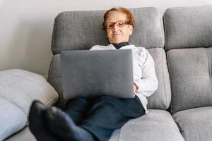 rustige senior vrouw browsen laptop in woonkamer foto