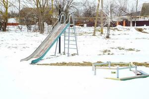 kinderen speelplaats in winter onder sneeuw. schommel, carrousel en schuiven. winter verwoesting foto