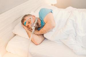slapende man met chronische ademhalingsproblemen overweegt cpap-machine in bed te gebruiken. gezondheidszorg, obstructieve slaapapneu-therapie, cpap, snurkconcept foto