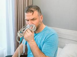 ongelukkige geschokte man met chronische ademhalingsproblemen verrast door het gebruik van een cpap-machine die op het bed in de slaapkamer zit. gezondheidszorg, cpap, obstructieve slaapapneu-therapie, snurkconcept foto