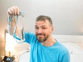 volwassen gelukkige man met chronische ademhalingsproblemen overweegt zittend op het bed in de slaapkamer met cpap-machine. gezondheidszorg, cpap, snurkconcept foto