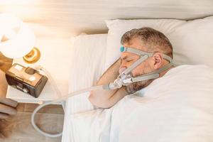 slapende man met chronische ademhalingsproblemen overweegt cpap-machine in bed te gebruiken. gezondheidszorg, obstructieve slaapapneu-therapie, cpap, snurkconcept foto