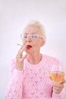 ouderwetse senior stijlvolle vrouw roken sigaret met glas witte wijn. slechte gewoonte, verslavingsconcept foto