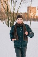 senior vrouw in hoed en sportieve jas joggen in sneeuw winter park. winter, leeftijd, sport, activiteit, seizoensconcept foto