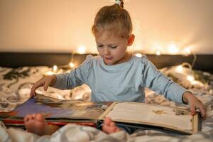 weinig meisje lezing knal omhoog boek in huis bed in Kerstmis milieu met lichten achtergrond. hoog kwaliteit foto