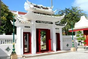 Chinese stijl van oude wit poort met dak, helder rood hout deur en licht blauw lucht achtergrond, wat ratcha orasaram ratchaworawihan, Thailand. foto