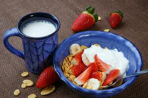 gezond ontbijt. cornflakes, vers aardbeien, banaan, yoghurt en melk foto
