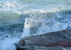 spatten van golven Aan de beton aan het strand promenade. steen stappen naar de zee foto