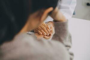 dokter en geduldig zittend in de buurt elk andere Bij de tafel in kliniek kantoor. de focus is Aan vrouw arts handen geruststellend vrouw, enkel en alleen handen, dichtbij omhoog. geneeskunde concept foto