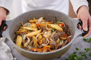 handen Holding braadpan met een typisch Peruaanse schotel gebeld lomo saltado. foto