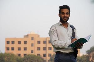 jonge mannelijke collagestudent die buiten op de campus staat en een boek leest foto